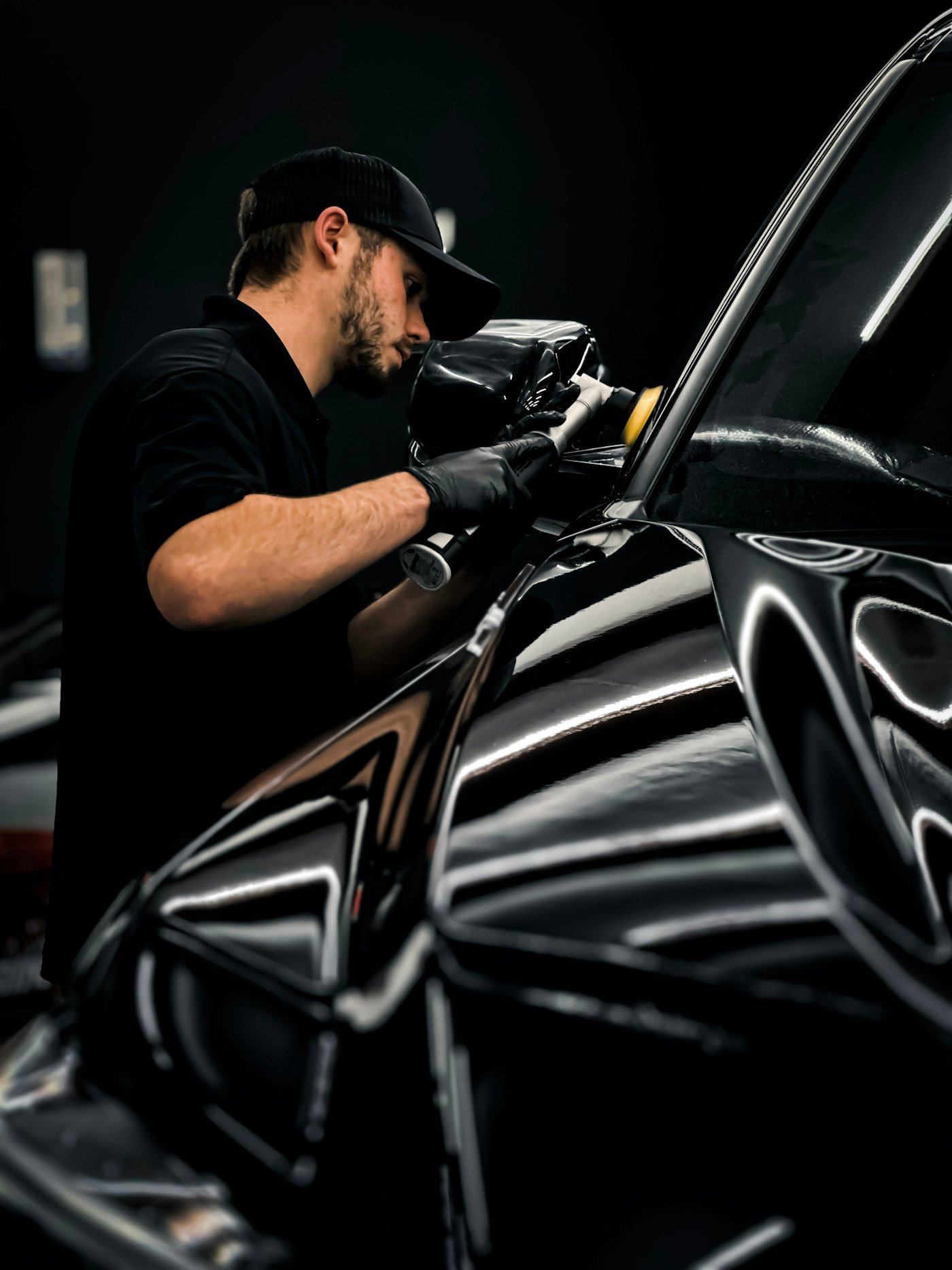 Detailer in black gloves hand-polishing the side of a black car
