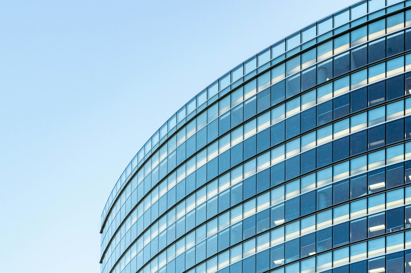 Curved glass office building reflecting a clear blue sky