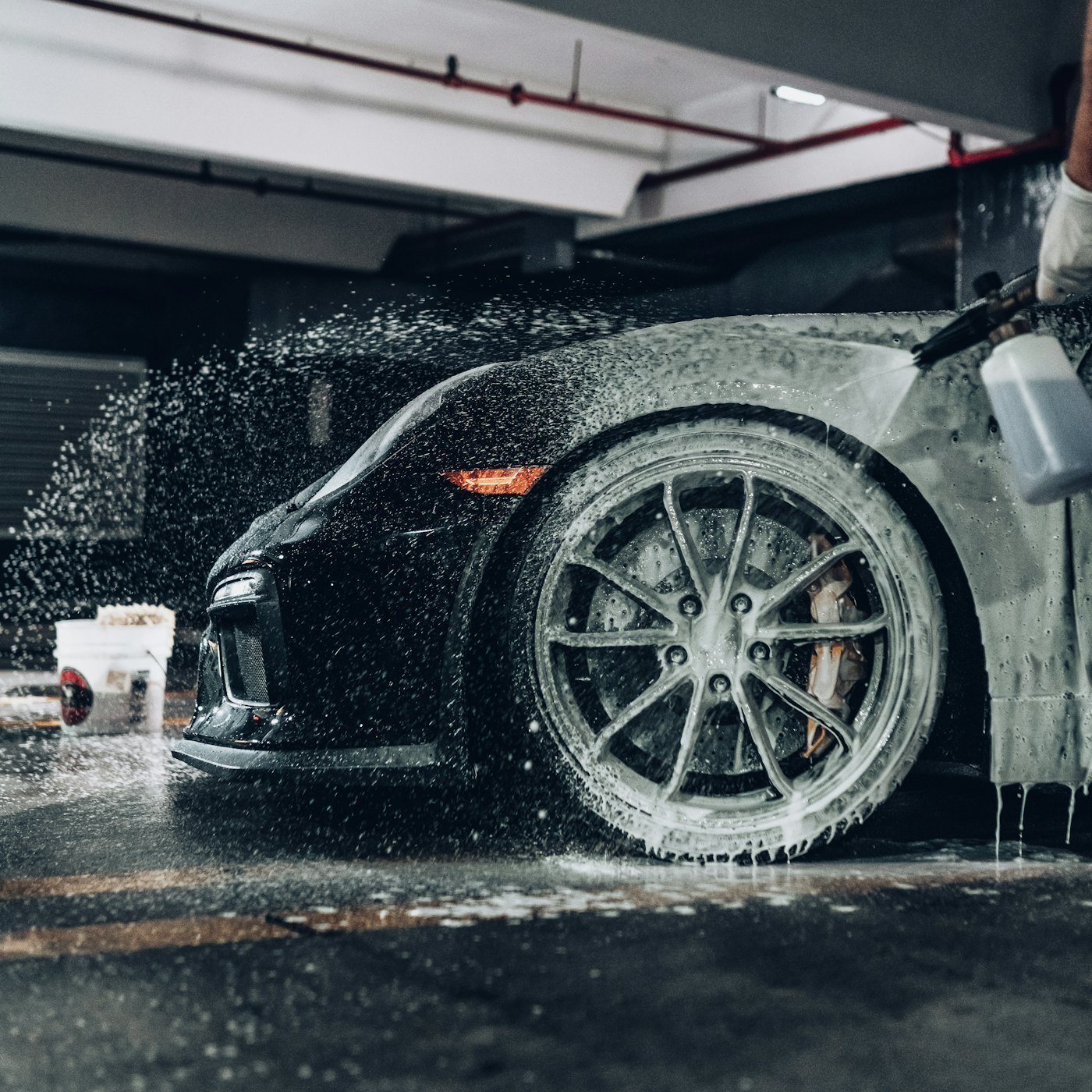 Black sports car covered in thick wash foam in a garage
