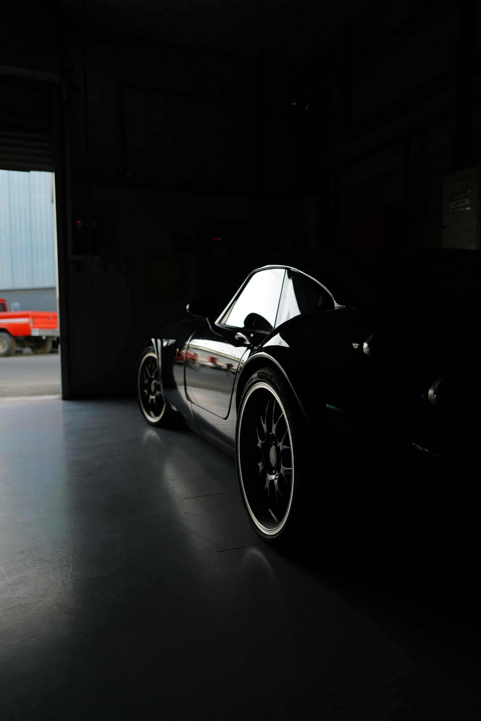 Glossy black sports car parked in a dark garage under a single light