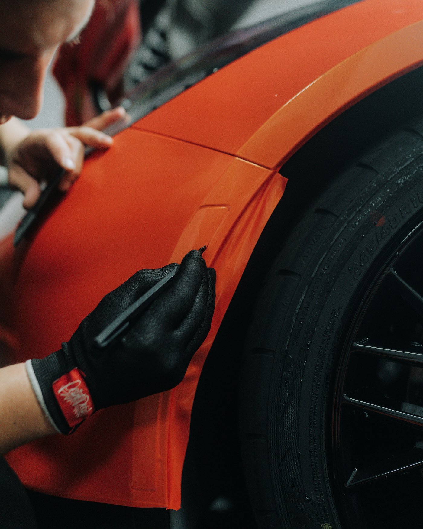 Gloved hands smoothing a sheet of film onto an orange car